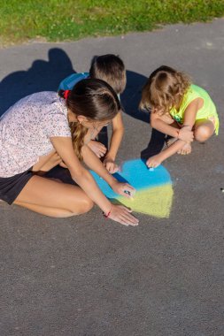 Çocuklar tebeşirle bir kalp çizer ve onu mavi ve sarıya boyarlar