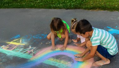 Çocuklar asfalta tebeşirle çizer. Bir gökkuşağı, bir ev, güneş, asfalta bulutlar çizilir..