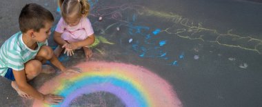 Oğlan ve kız asfalta tebeşirle gökkuşağı çiziyor.
