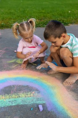 Oğlan ve kız asfalta tebeşirle gökkuşağı çiziyor.