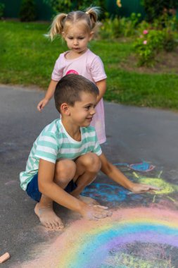 Çocuklar asfalta tebeşirle çizer. Bir gökkuşağı, bir ev, güneş, asfalta bulutlar çizilmiş..