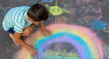 Tebeşirle çizen çocuk gökkuşağı ve asfaltta bir ev.