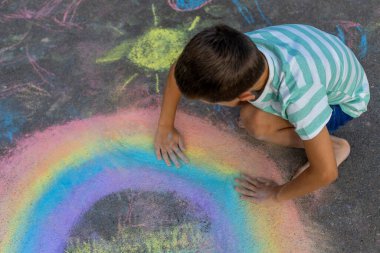Tebeşirle çizen çocuk gökkuşağı ve asfaltta bir ev.