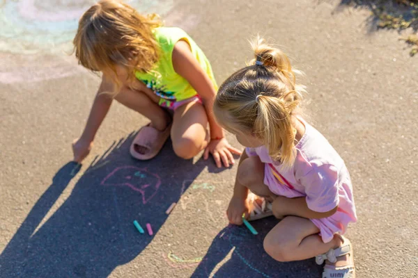 İki küçük kız asfalta tebeşir çiziyor.
