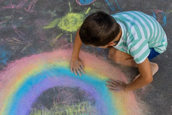 Tebeşirle çizen çocuk gökkuşağı ve asfaltta bir ev.