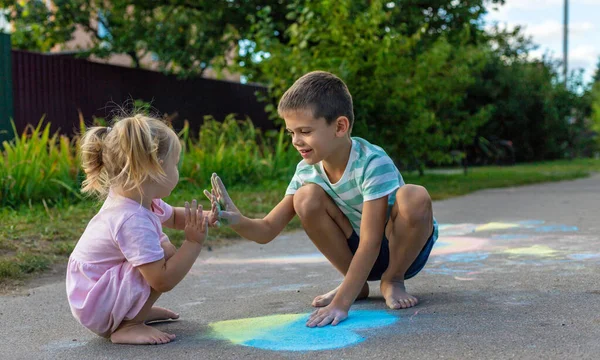 Bir erkek ve bir kız tebeşirle bir kalp çiz ve onu mavi ve sarıya boya..