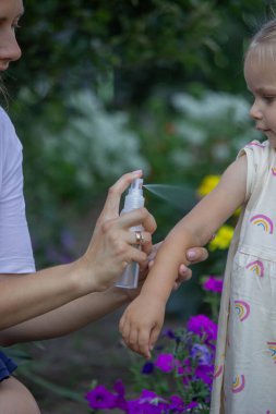 Anne, çocukların kollarına böcek kovucu sprey sıkıyor. Seçici odak.