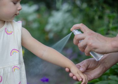 Anne, çocukların kollarına böcek kovucu sprey sıkıyor. Seçici odak.