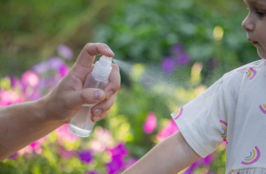 Babam çocuğun eline böcek kovucu sprey sıkıyor. Seçici odak.