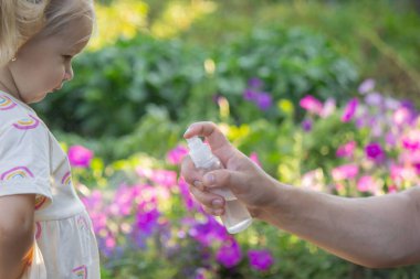 Babam çocuğun eline böcek kovucu sprey sıkıyor. Seçici odak.
