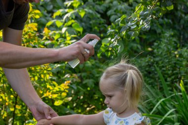 Babam çocuğun eline böcek kovucu sprey sıkıyor. Seçici odak.