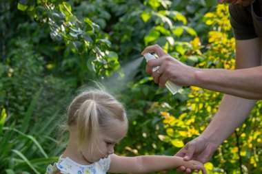 Babam çocuğun eline böcek kovucu sprey sıkıyor. Seçici odak.