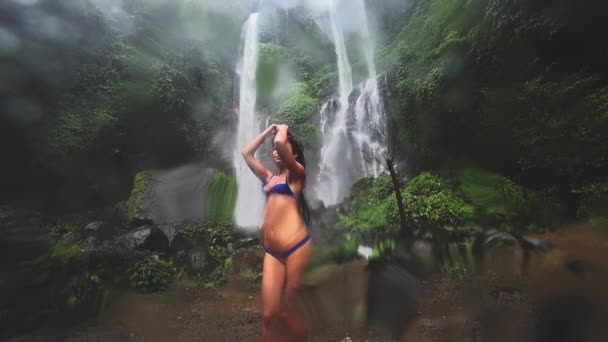 Молодая сексуальная женщина смотрит на водопад в джунглях. Экотуризм — стоковое видео