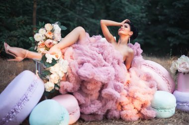 Seksi kadın moda elbise çarpıcı pembe giymiş, büyük Fransız Macarons ve balonlar ve taze çiçek süslemeleri çevrili