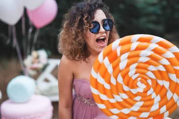 Szokatlan csípő nő eszik egy nagy narancssárga lollypop neki Party — Stock Fotó