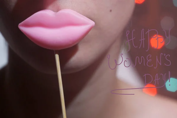 美女欢乐年轻有趣的时装模特女孩拿着大粉红色的嘴唇在一根棍子微笑 3月8日签署快乐的妇女节的概念 Bokeh 灯背景下 — 图库照片