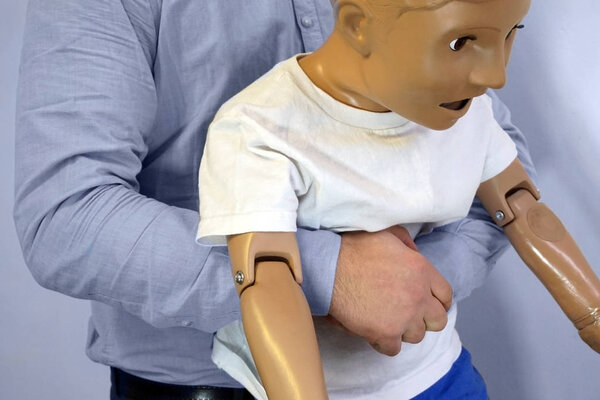 Abdominal thrusts (the Heimlich maneuver or Heimlich manoeuvre) on a simulation mannequin child dummy during medical training Basic Life Support