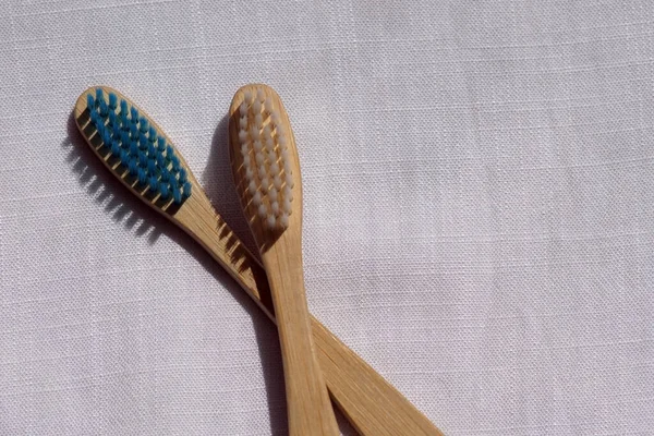 Close up of the Eco-friendly white and blue bamboo toothbrushes on a white linen background. Natural organic bathroom beauty product concept. Flat lay, top view, copy space