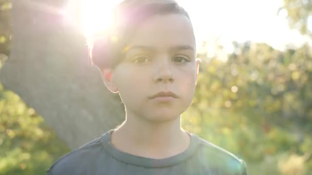 Niño adolescente mirando a la cámara. Detrás de él el sol de la tarde. — Vídeo de stock