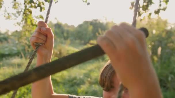 Un adolescent se balance sur une balançoire et regarde la caméra. — Video