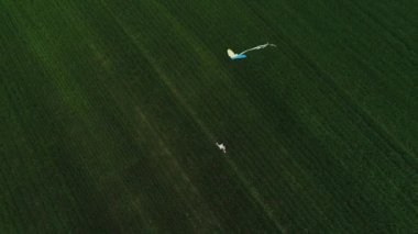 Çocuk peşinde bir uçurtmayla yeşil bir arazide koşuyor..