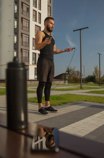 Genç bir adam ip atlama ile ayakta duruyor. Görüntüsü akıllı telefondadır..