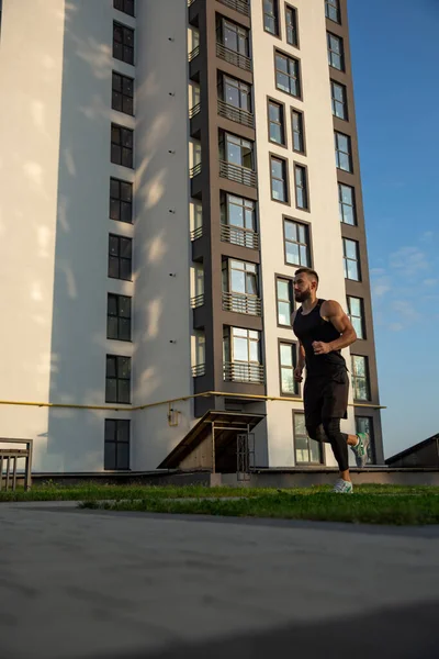 Ochtend joggen van een jonge loper op de achtergrond van een hoogbouw. — Stockfoto