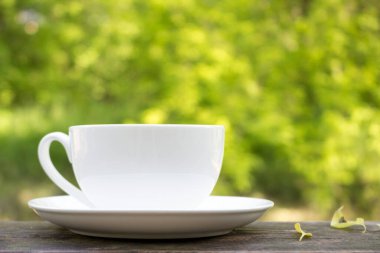 Güneşli bir yaz gününde tahta bir masada beyaz bir kupa. Günün başlangıcına ait huzurlu bir resim. Güzel bir günün sabahı.