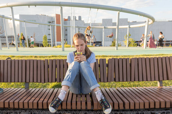 teenage girl uses smartphone while sitting on a Park bench, jeans modern clothing