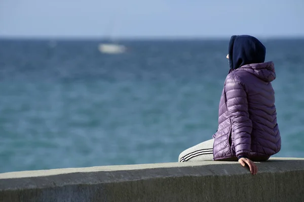 The girl sits on the pier and looks at the sea