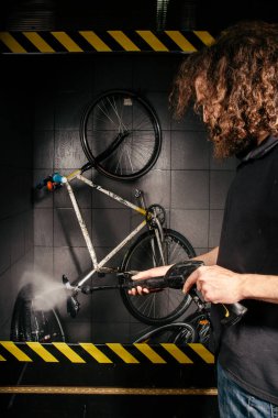 Bir bisiklet atölyesinde profesyonel yıkama hizmetleri. Otomatik elektrikli su pompası ile bisiklet temizlik yapan el genç beyaz şık erkek Close-up. Spreyler dağılım düşük basınç.