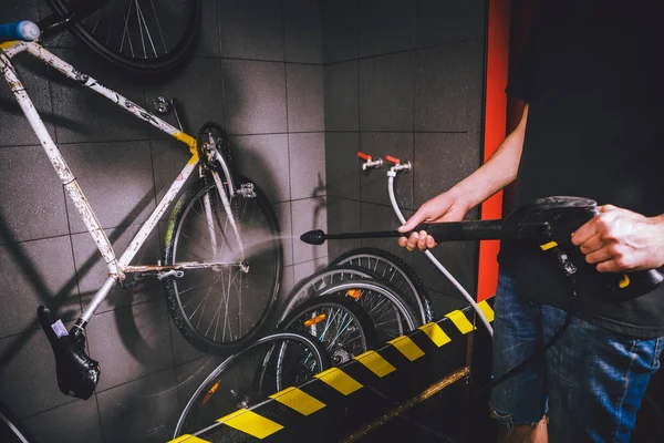 Bisiklet atölyesinde profesyonel yıkama hizmetleri. Bir otomatik elektrikli su pompası ile bisiklet temizlik yapan el genç beyaz şık erkek Close-up. Spreyler dağılım düşük basınç.