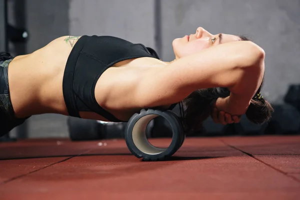 Güzel genç kafkas kadın sporcumuz bir köpük rulo Masaj kas ve sırt ağrısı germe gevşeme için kullanır. Kız spor salonu yeşil spor ayakkabı T-shirt ve tayt