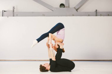 Paspaslar üzerinde beyaz bir spor salonunda akrobatik yoga uygulamak genç bir beyaz erkek ve kadın çift. Onlar yıldız poz vardır.
