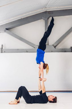 Spor ve dönüm temasıdır. Paspaslar üzerinde beyaz bir spor salonunda akrobatik yoga uygulamak genç bir beyaz erkek ve kadın çift. bir adam sırt üstü yatıyor ve bir kadın genişletilmiş silah tutar. El poz.