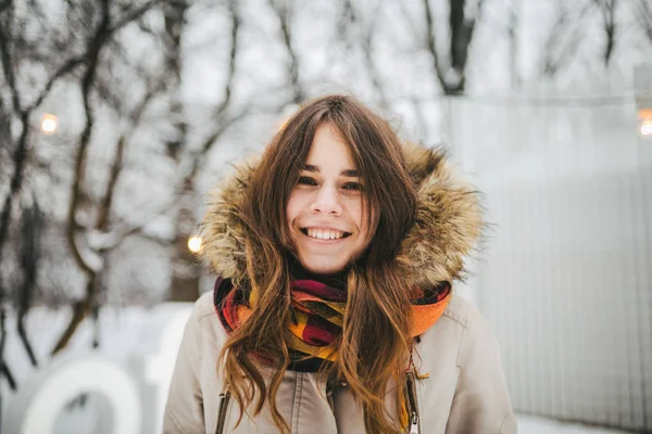 Tema Kışın hafta sonu tatildir. Kürk kot pantolon ve ceket kukuleta ile parkta kar ayakta ve gülümseyen güzel genç beyaz kadın.