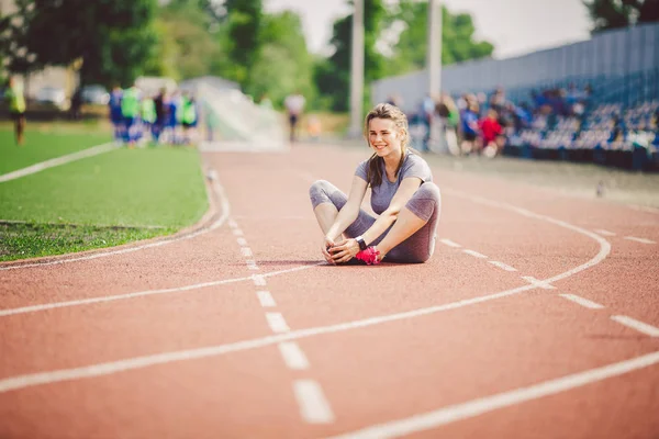 Kuyruk ve egzersizleri yapıyor, ısınma ve eğitim güneşli bir yaz aylarında çalışan Stadyumu, Kırmızı lastik parça önce kasları ısınma büyük göğüsler uzun saçlı güzel genç bir beyaz kadın.