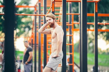 Konu spor sokak egzersiz yakışıklı genç beyaz adamla bir çıplak göğüslü uzun kızıl saçlı ve açık spor alanı, spor salonu açık havada poz sakal ile kas. Seksi bir adam saçını dokunur