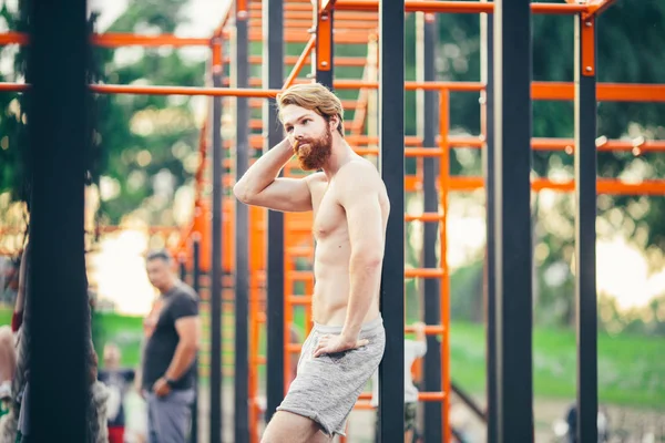 Konu spor sokak egzersiz yakışıklı genç beyaz adamla bir çıplak göğüslü uzun kızıl saçlı ve açık spor alanı, spor salonu açık havada poz sakal ile kas. Seksi bir adam saçını dokunur