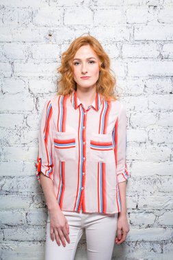 Kırmızı kıvırcık saçlı ve çilli güzel genç kadın öğrenciyle gri renkli bir tuğla duvara yaslanmış. Kırmızı çizgili bir gömlek ve beyaz pantolon giymiş