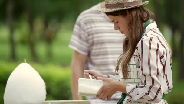 视频主题是小企业烹饪糖果 一个年轻的白种女人与一个围裙商人在帽子插座的所有者做糖果牙线 仙女牙线或棉花糖在夏天公园里 — 图库视频影像