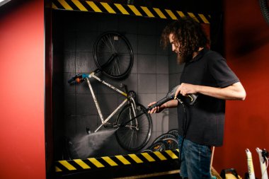 Bir bisiklet atölyesinde profesyonel yıkama hizmetleri. Otomatik elektrikli su pompası ile bisiklet temizlik yapan el genç beyaz şık erkek Close-up. Spreyler dağılım düşük basınç.