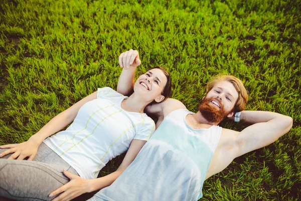 スポーツと健康的なライフ スタイル テーマです 若い男性と女性のカップルは スポーツをプレイした後緑の草に背 パックで芝生の上に横たわって休んでいます 家族の合同訓練 — ストック写真