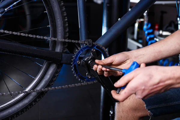 A close-up of a male bicycle mechanic's hand in the workshop uses a screwdriver tool to adjust and repair the bicycle crank assembly, the front bike stars in the bicycle store