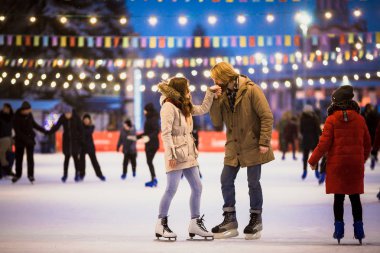Uzun saçlı sarışın saçlı beyaz adam genç çift tr ve eğlenceli, aktif tarihi buz pateni Buz arenada akşam şehir meydanında Noel arifesinde kışın sakal ve güzel bir kadın var