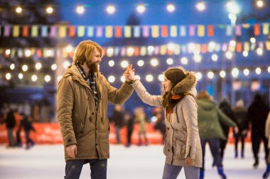 Uzun saçlı sarışın saçlı beyaz adam genç çift tr ve eğlenceli, aktif tarihi buz pateni Buz arenada akşam şehir meydanında Noel arifesinde kışın sakal ve güzel bir kadın var