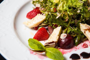 kiraz, çilek ve siyah bir zemin üzerine beyaz büyük bir tabak peynirli salata