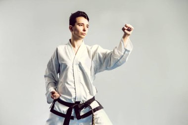 Kız karate gri arka planı stüdyosunda kimono uygun. Kadın çocuk judo veya karate gösterir beyaz siyah kuşak ile Tekdüzen stans. Bireysel savaş sanatı spor. Tam vücut portre