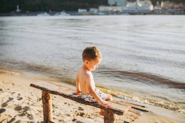 suya yakın sahilde sırtı ile ahşap bir bankta oturan ve Kiev şehir onun el ileri yönde-fon karşı gösterilen çocuk çocuk.