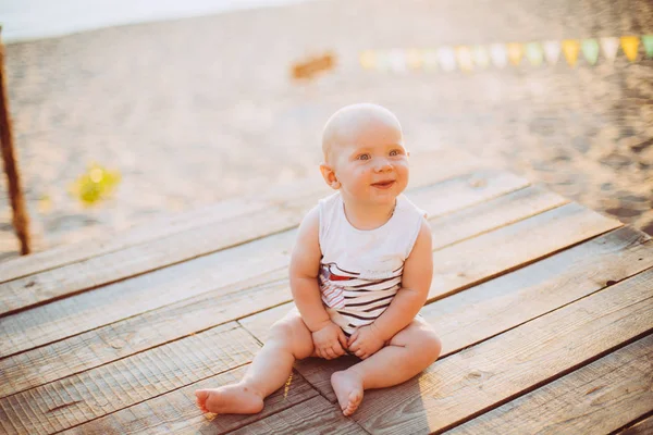 夏の日の夕暮れ時のウッドデッキは ストライプの服で桟橋 川を背景に砂浜で池の近くの化合物に座っている少年 年金髪の子 — ストック写真